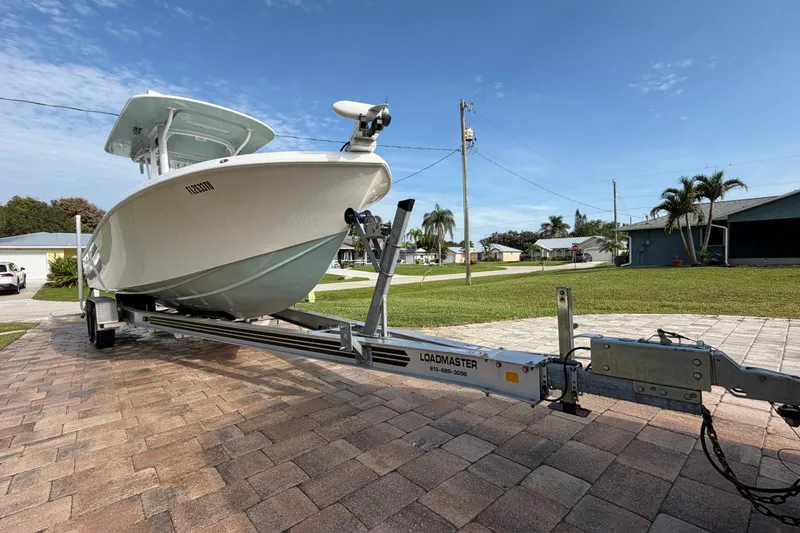 Slide: The Image of 2024 Bluewater BW 25T boat on Loadmaster trailer, parked on a paved driveway under a clear sky. - 63