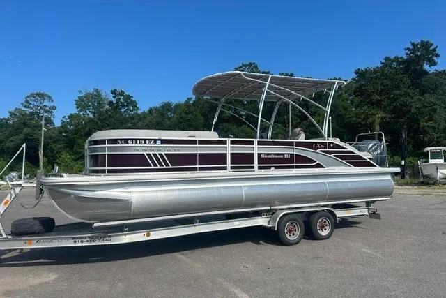 The Image of 2023 Bennington 26LXSBSP pontoon boat on trailer, parked outdoors under clear sky. - 1
