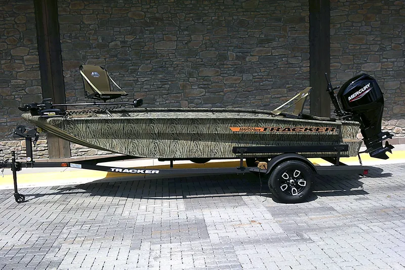 The Image of 2026 Tracker Grizzly 1756 T Marsh boat on trailer, camo design, parked on brick pavement. - 0