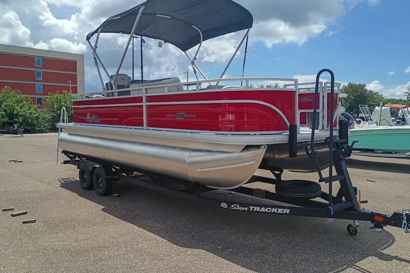 The Image of 2027 Sun Tracker Fishin' Barge 22 DLX pontoon boat on trailer, parked outdoors. - 0