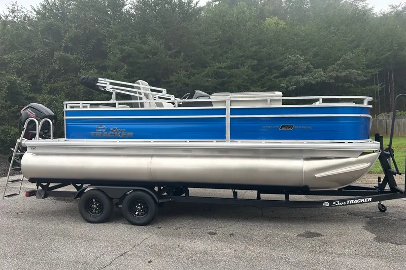 The Image of 2027 Sun Tracker Fishin' Barge 20 DLX pontoon boat on trailer, parked outdoors. - 0