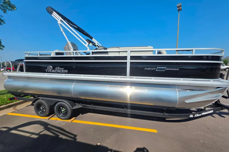 The Image of 2027 Sun Tracker Fishin' Barge 22 DLX pontoon boat on trailer in parking lot. - 0