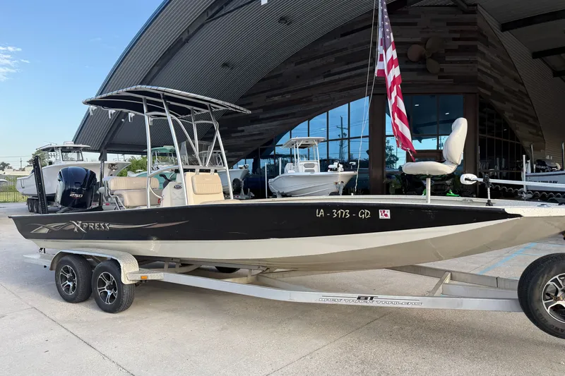 Slide: The Image of 2015 Xpress H24 Bay boat on trailer with American flag, parked outside a modern building. - 22