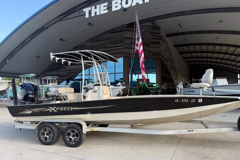 Slide: The Image of 2015 Xpress H24 Bay boat on trailer, parked outside a showroom with an American flag. - 21
