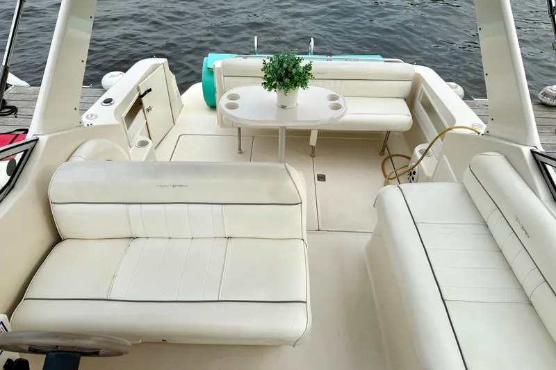 Slide: The Image of 1999 Monterey 296 Cruiser boat interior with white seating and table, docked by the water. - 3