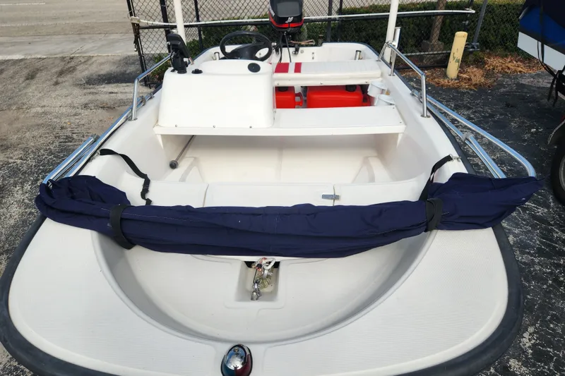 Slide: The Image of 2000 Boston Whaler Sport 13 boat with steering console and seating, parked on pavement. - 2