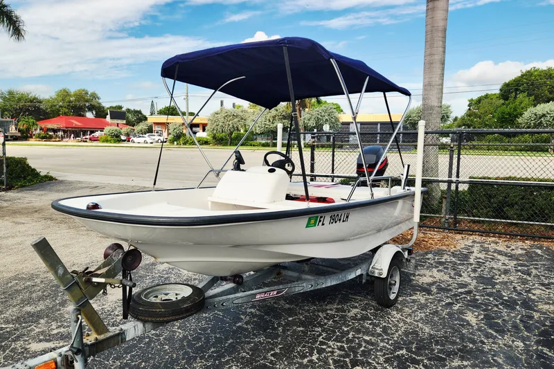 Slide: The Image of 2000 Boston Whaler Sport 13 boat on trailer with blue canopy, parked outdoors. - 1