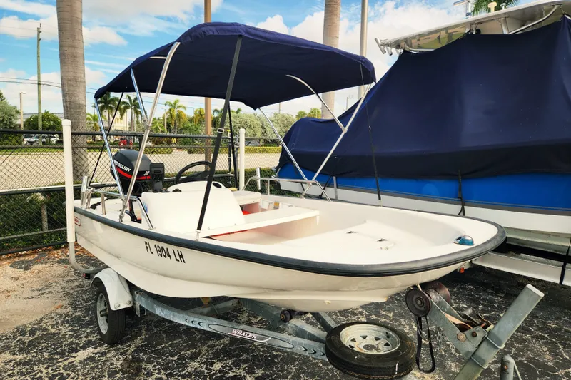 The Image of 2000 Boston Whaler Sport 13 boat on trailer with canopy, parked outdoors. - 0