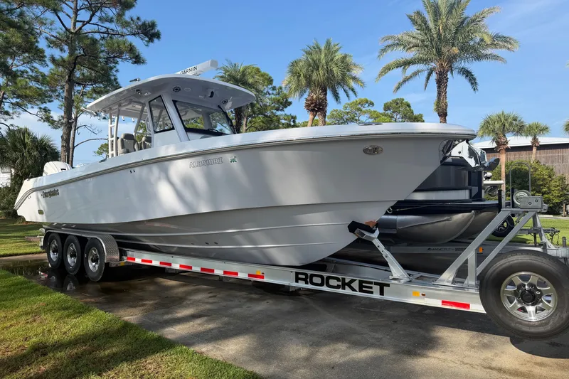 The Image of 2021 Everglades 335 Center Console boat on trailer, surrounded by palm trees. - 0