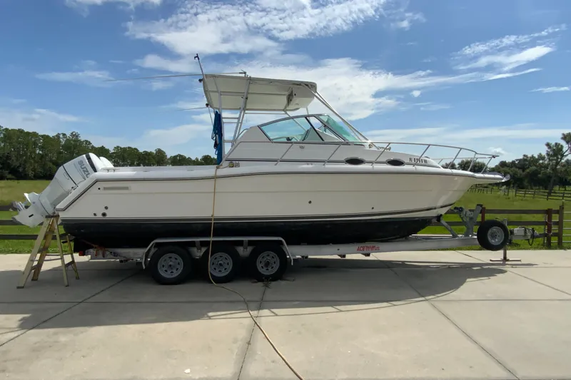 The Image of 2001 Stamas 290 Express boat on trailer, parked outdoors under blue sky. - 0