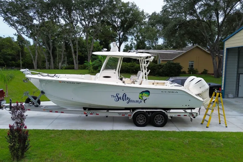 The Image of 2020 Cobia 301 Center Console boat on trailer, parked in driveway with trees in background. - 0