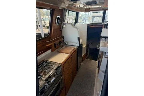 Slide: The Image of Interior of 2026 Ranger Tugs R-27, featuring a compact kitchen with stove and seating area. - 6