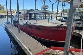 The Image of 2026 Ranger Tugs R-27 boat docked in a marina, red hull, covered slip. - 1