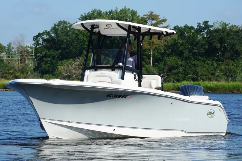 Slide: The Image of 2022 Sea Hunt Ultra 234 boat cruising on a calm lake with lush greenery. - 4