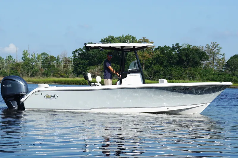 Slide: The Image of 2022 Sea Hunt Ultra 234 boat on calm water with lush greenery background. - 2