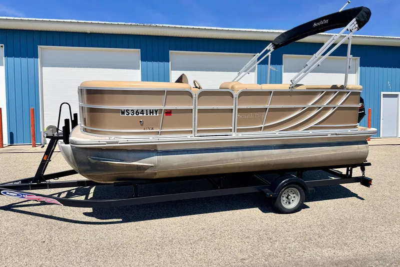 Slide: The Image of 2013 South Bay 417 CR pontoon boat on trailer, parked outside blue building. - 5