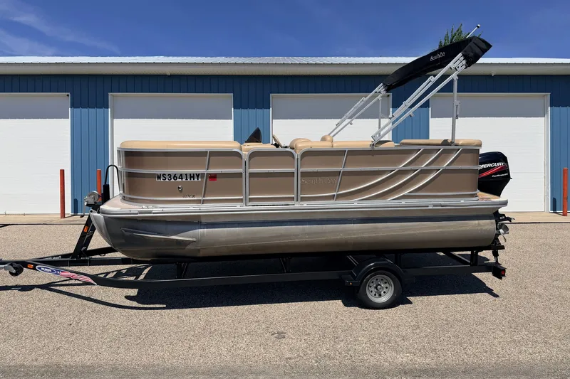 Slide: The Image of 2013 South Bay 417 CR pontoon boat on trailer, parked outside blue building. - 1