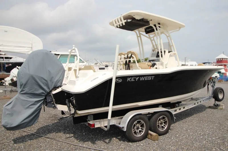 The Image of 2018 Key West 239 FS boat on trailer, black hull, covered engine, parked outdoors. - 0
