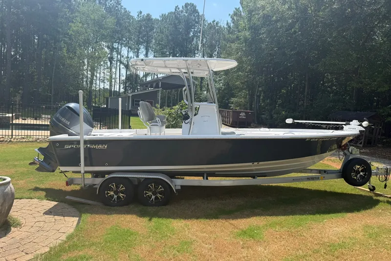 The Image of 2022 Sportsman Masters 227 Bay Boat on trailer, parked on grass, surrounded by trees. - 0