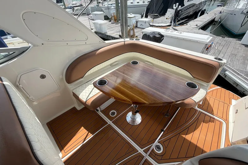 Slide: The Image of 2008 Bayliner 300 boat interior with wood table, cushioned seating, and cup holders at marina. - 6