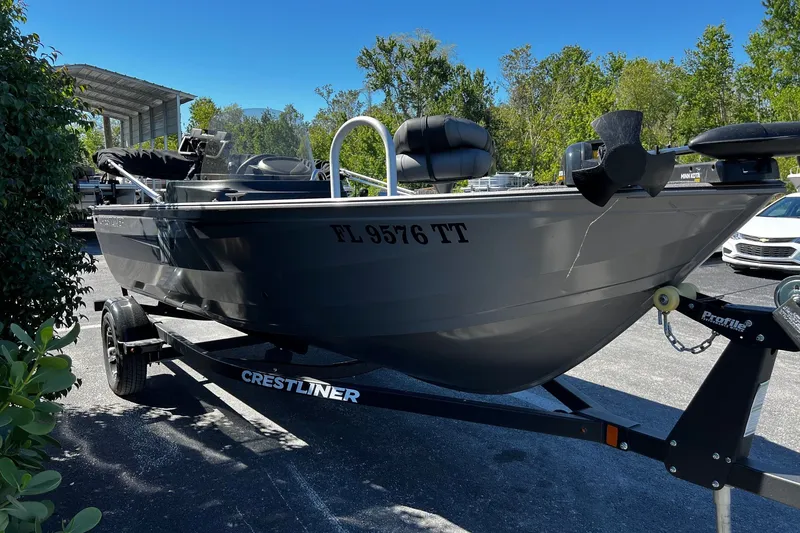 Slide: The Image of 2023 Crestliner 1600 Vision boat on trailer, parked outdoors with trees in background. - 2