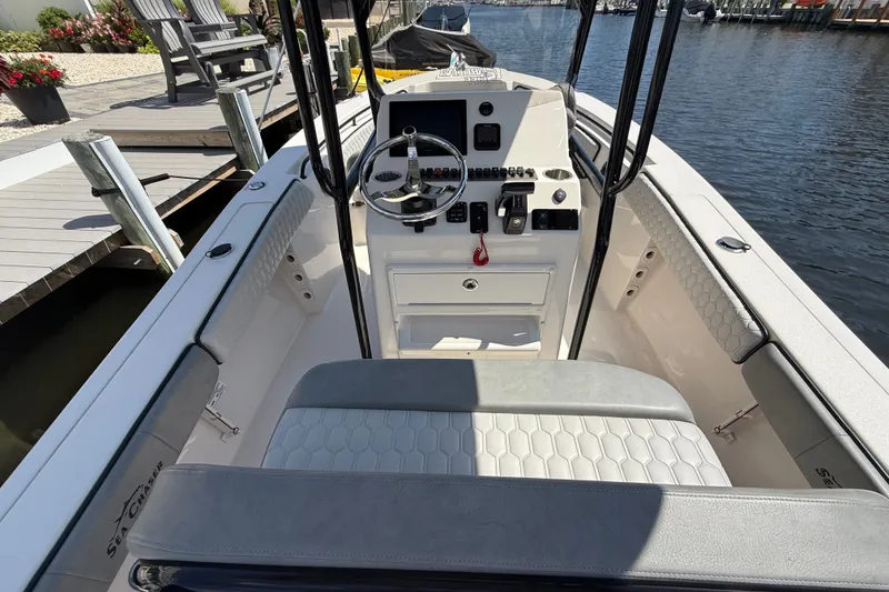Slide: The Image of 2025 Sea Chaser 22 HFC boat interior with steering console and seating, docked by the water. - 6