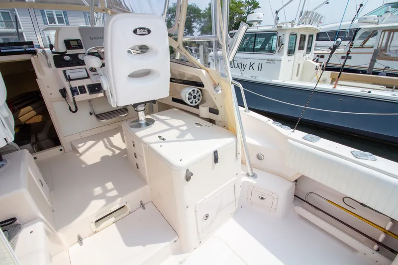 Slide: The Image of The image shows the cockpit of a 2004 Grady-White Marlin 300. It features a helm station, seating, and rod holders. Other boats are visible in the background. - 31