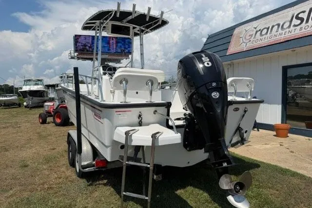 Slide: The Image of 2013 Boston Whaler 21 Montauk boat with outboard motor, parked on grass near a building. - 2