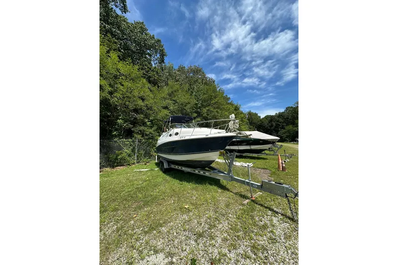 Slide: The Image of 2006 Larson Cabrio 240 boat on trailer, parked on grassy area under blue sky. - 4