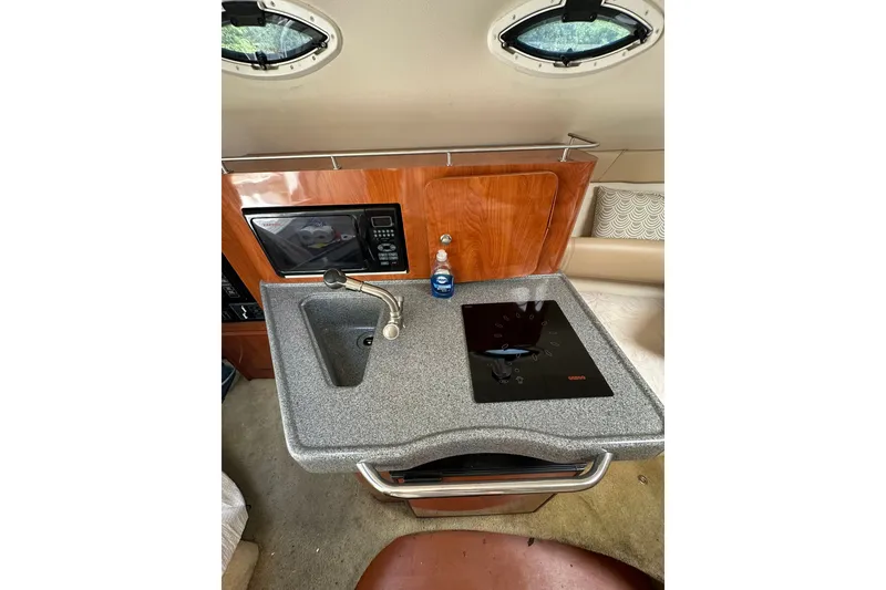 Slide: The Image of 2006 Larson Cabrio 240 boat interior with kitchenette, featuring sink, stove, and microwave. - 12