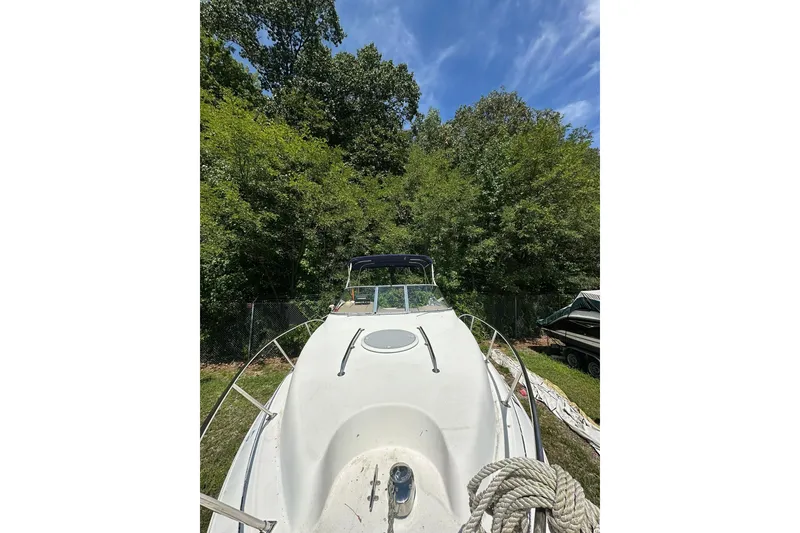 Slide: The Image of 2006 Larson Cabrio 240 boat docked near lush green trees under a clear blue sky. - 6