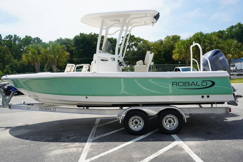The Image of 2027 Robalo 226 Cayman boat on trailer, green hull, parked outdoors. - 1