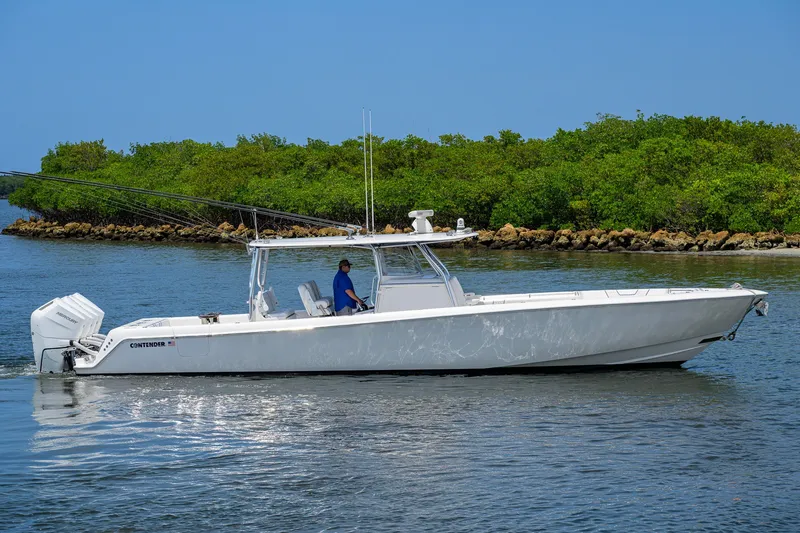 The Image of 2023 Contender 44 ST boat cruising on calm water near lush green shoreline. - 0