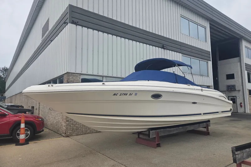 The Image of 2001 Sea Ray 290 Bow Rider boat with blue canopy, displayed outside a warehouse. - 0