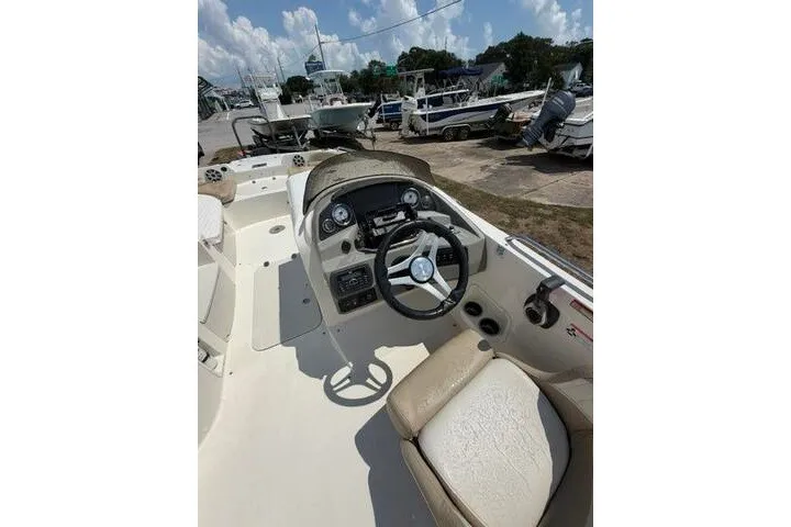 Slide: The Image of 2018 Stingray 212 SC boat interior with steering wheel and dashboard, parked outdoors. - 22