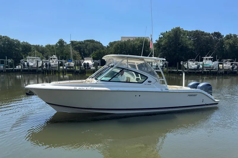 The Image of 2021 Pursuit DC 266 Dual Console boat on calm water, surrounded by trees and docks. - 0