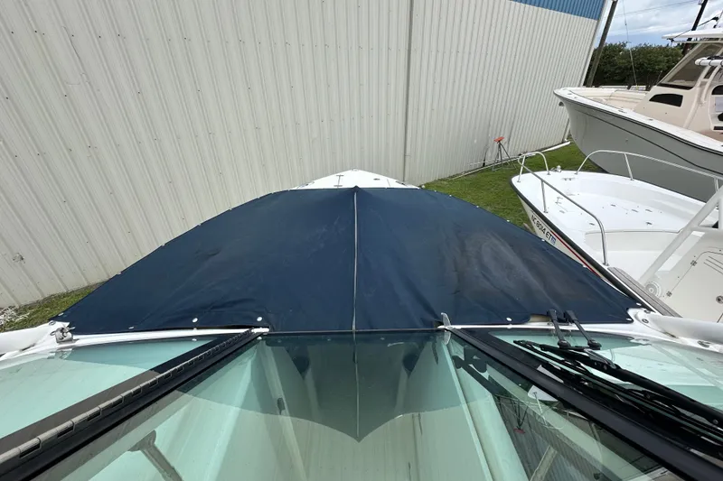 Slide: The Image of 2021 Pursuit DC 266 Dual Console boat with a blue cover, parked near a metal building. - 16