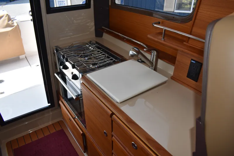 Slide: The Image of 2019 Ranger Tugs R-27 galley with stove, sink, and wooden cabinetry. - 35