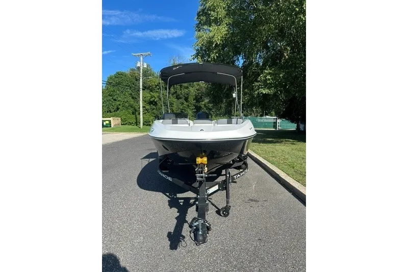 Slide: The Image of 2027 Tahoe T16 boat on trailer, parked on a sunny road with trees in the background. - 2