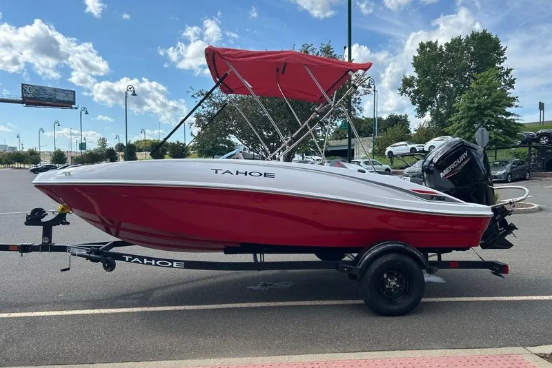 Slide: The Image of Red and white 2027 Tahoe T16 boat on trailer with canopy, parked outdoors. - 1