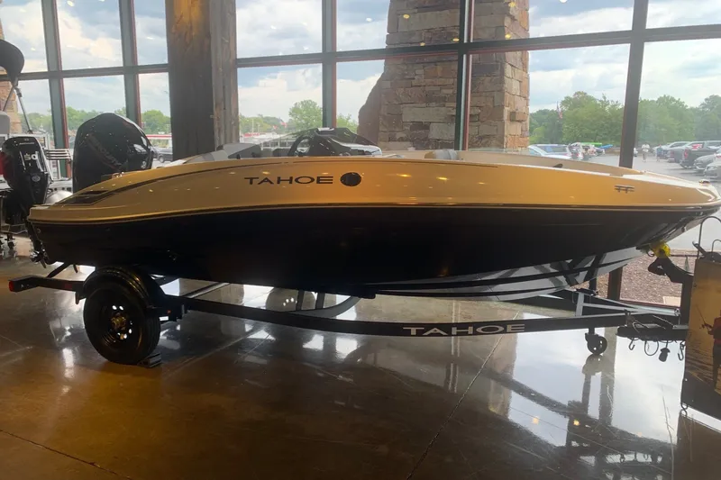The Image of 2027 Tahoe T16 boat displayed indoors with trailer, large windows in background. - 0
