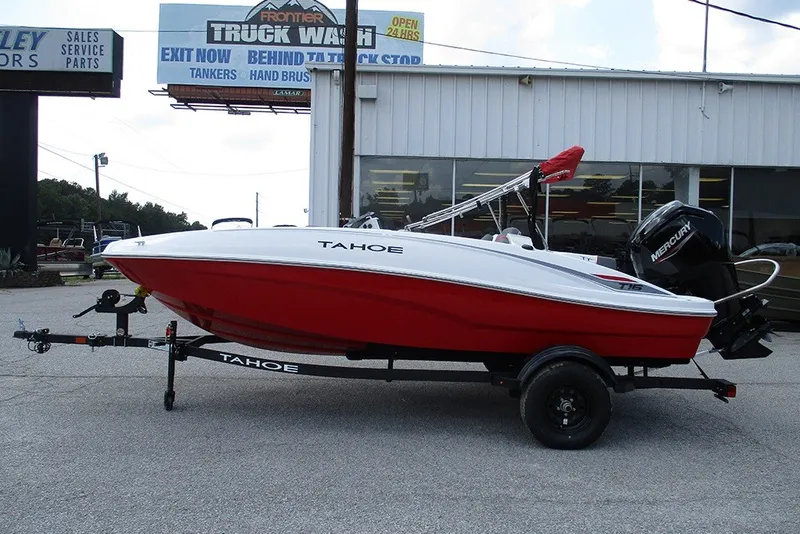 The Image of 2027 Tahoe T16 boat with red hull on trailer, parked outside dealership. - 1