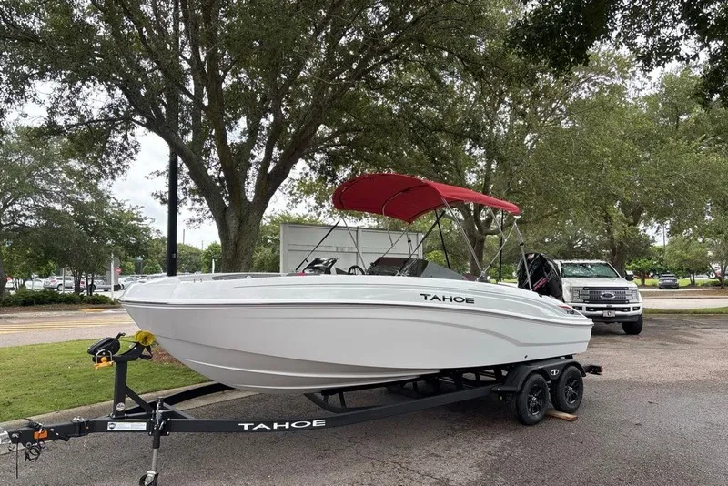 Slide: The Image of 2027 Tahoe T21 boat with red canopy on trailer, parked outdoors. - 2