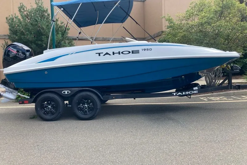 The Image of 2027 Tahoe 1950 boat on trailer, blue and white design, parked outdoors. - 0