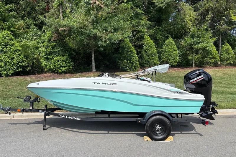 The Image of 2027 Tahoe T16 boat with Mercury engine on trailer, parked by lush greenery. - 0