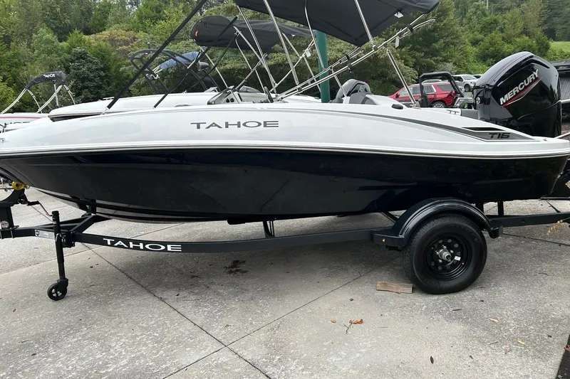 The Image of A white and black 2027 Tahoe T16 boat on a trailer, surrounded by trees. - 0