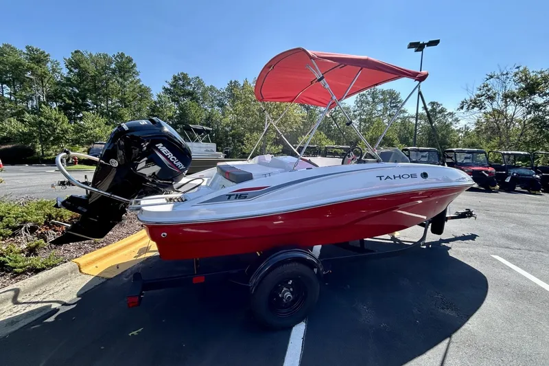 Slide: The Image of 2027 Tahoe T16 boat with red hull and canopy, parked outdoors. - 2