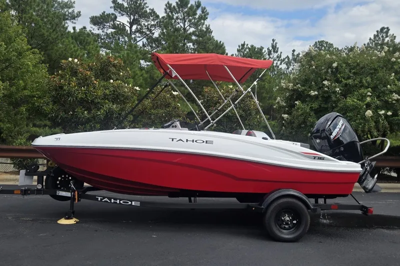 The Image of 2027 Tahoe T16 boat with red hull and canopy on a trailer, parked outdoors. - 0