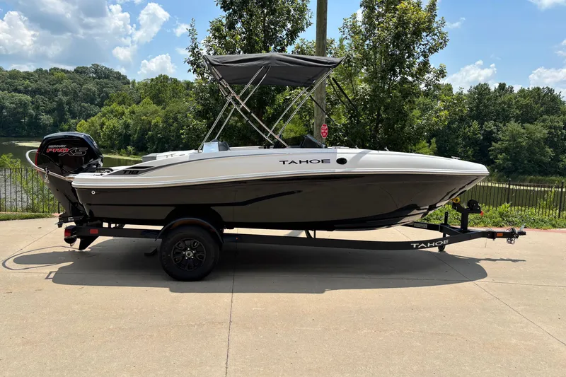 The Image of 2027 Tahoe T18 boat on trailer, parked near a scenic lake with lush greenery. - 0
