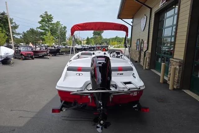 Slide: The Image of 2027 Tahoe T18 boat with red canopy, parked outside a building. - 2